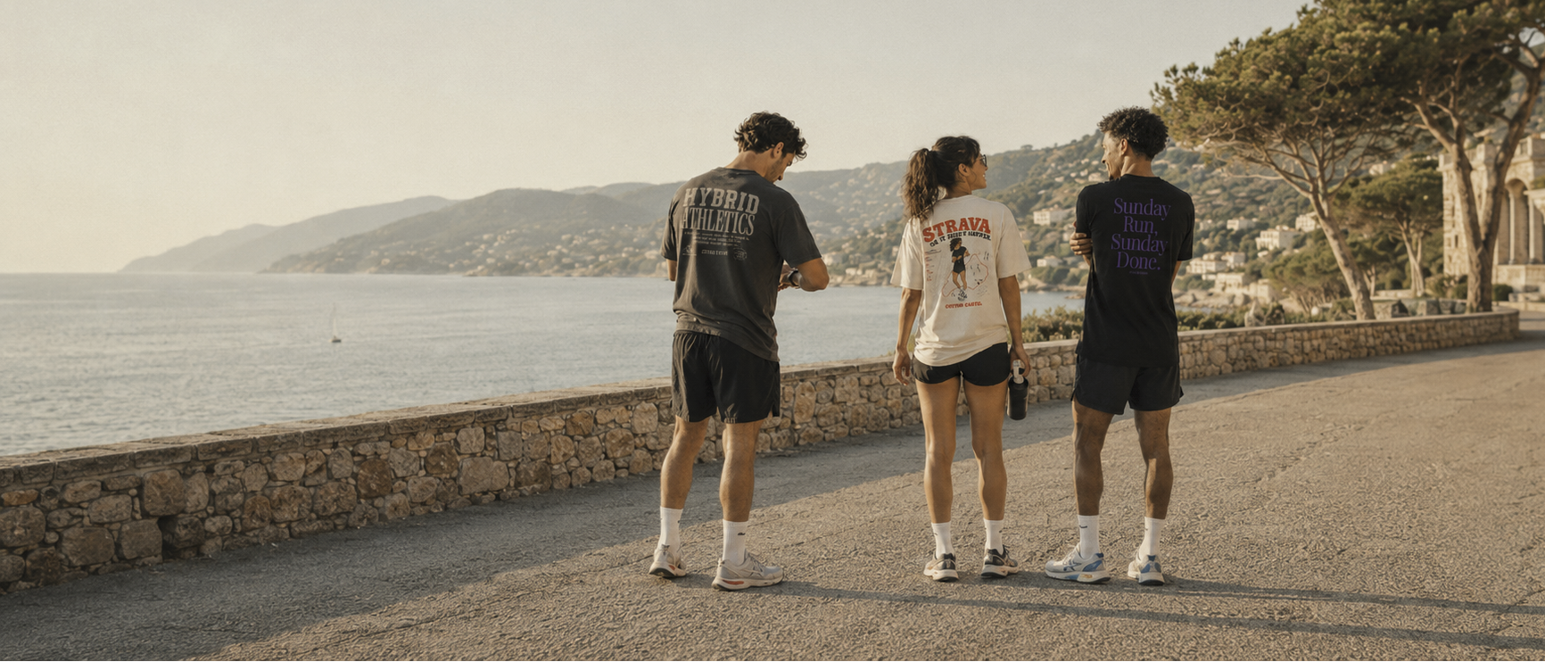 Three people walking along a scenic coastal path with ocean and mountains in the background.